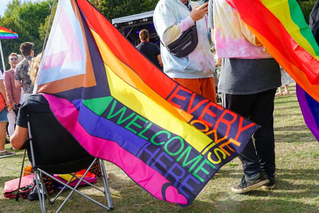 A photo of someone holding a rainbow flag saying Everyone Is Welcome Here